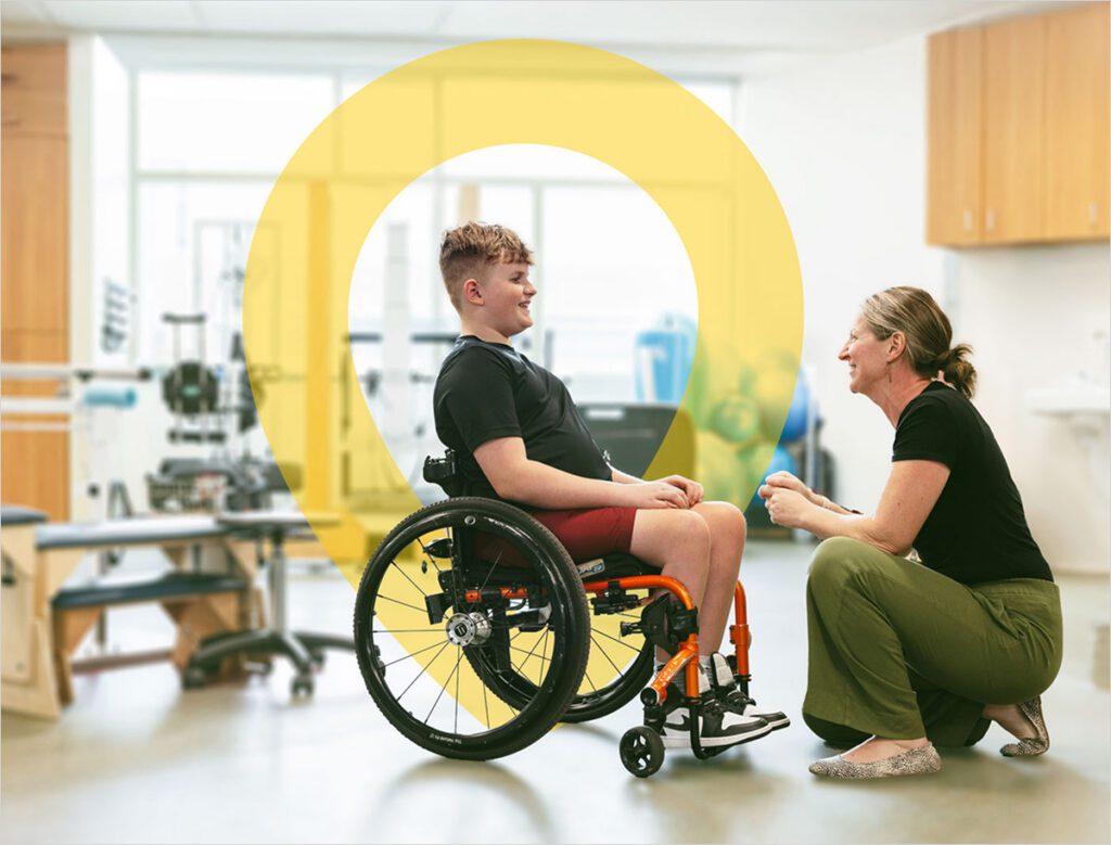 Child in a wheelchair talking with an adult in a therapy room.