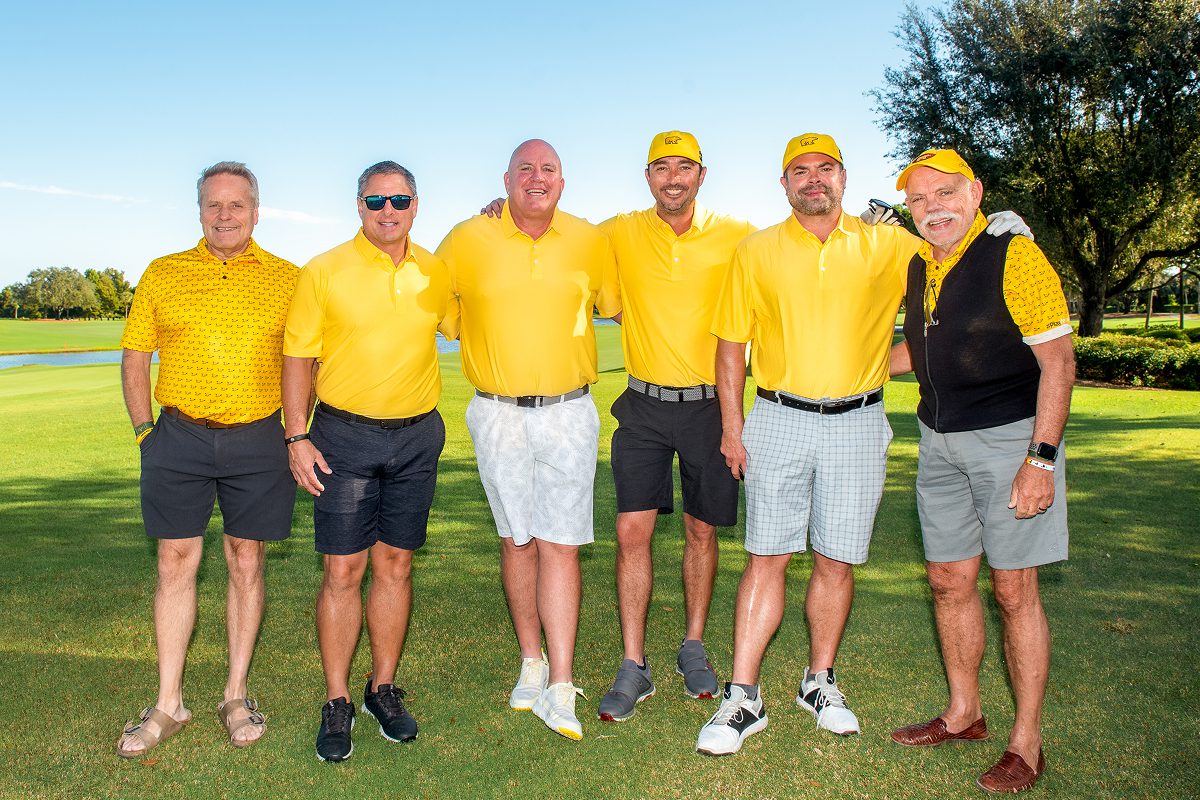 Six men posing together on a golf course, all wearing yellow Play Yellow polo shirts and yellow Golden Bear hats.
