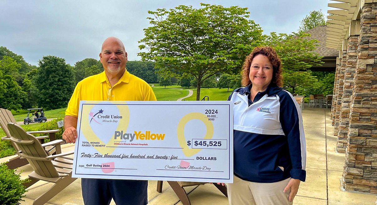 Two people holding a Play Yellow donation check for $45,525 at a golf outing.