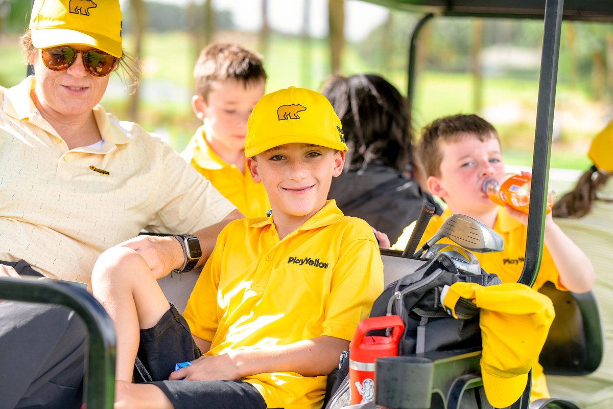 Young Play Yellow champion riding in a golf cart with other participants.