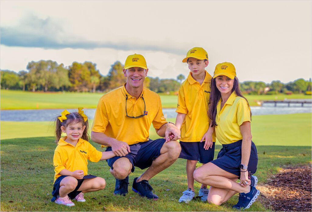 A family of four, including two young children, posing on a golf course; everyone is wearing yellow Play Yellow polo shirts and yellow Golden Bear hats.