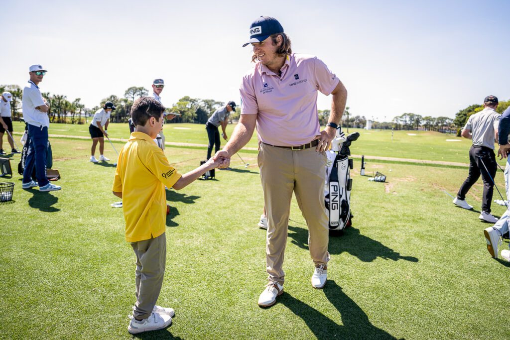 Young Play Yellow champion shaking hands with a golfer on a golf course.