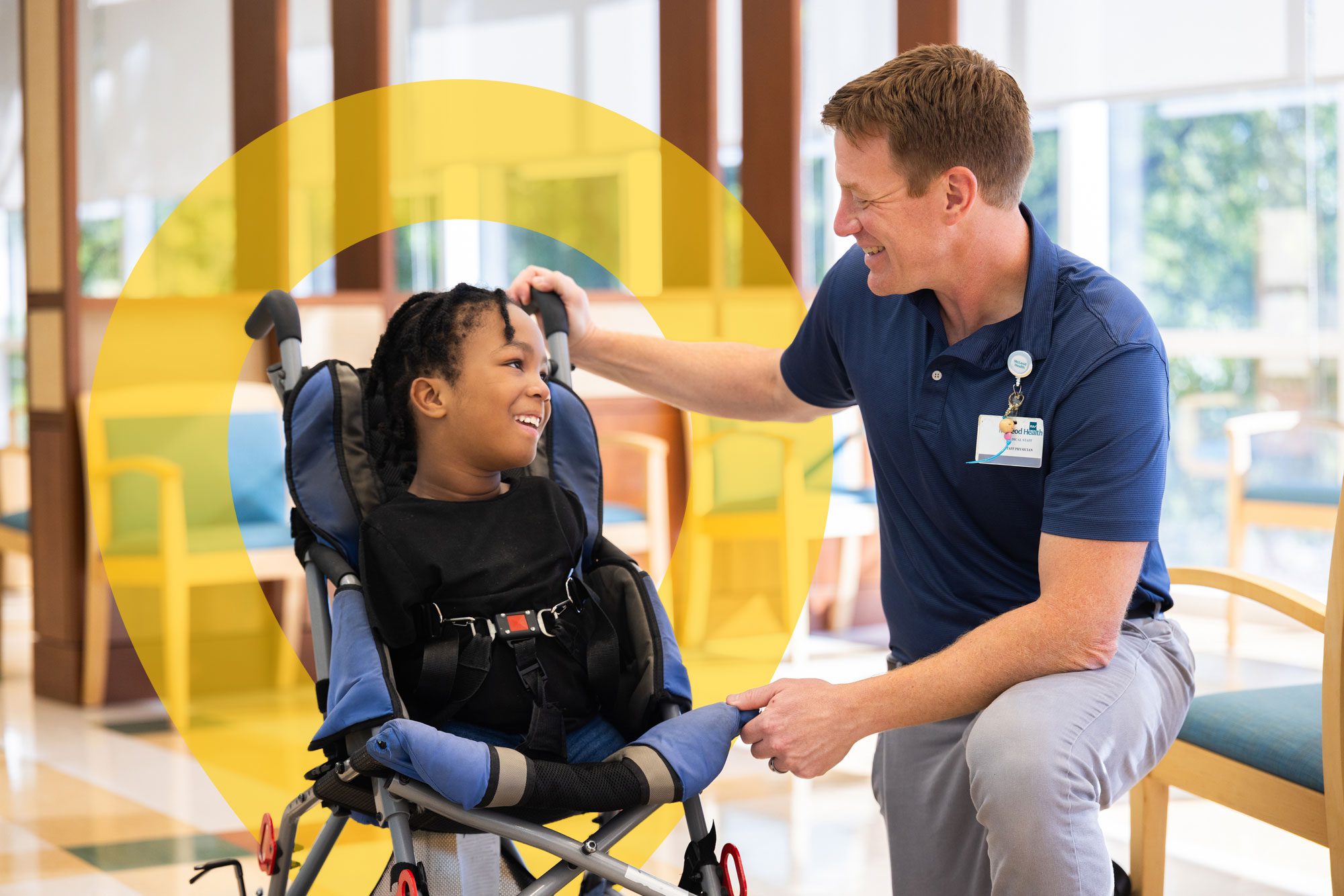 Child in a wheelchair smiling with a hospital staff member.